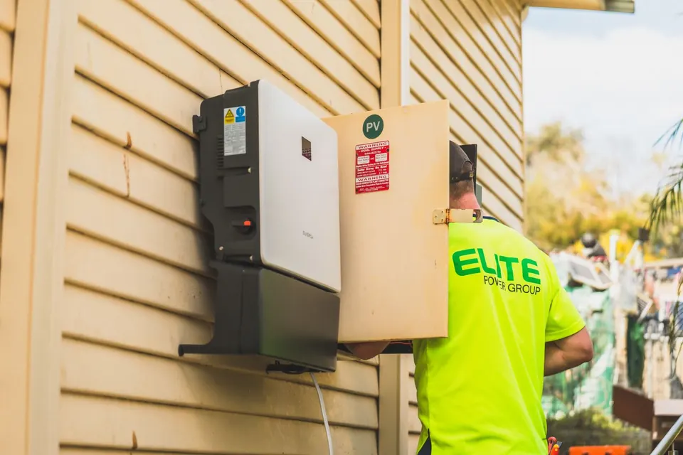 Electrician from Elite Power Group installing a solar inverter outside.